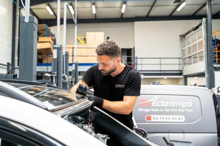 Technicien Éclatemps effectuant le remplacement d'un pare-brise dans un garage automobile.
